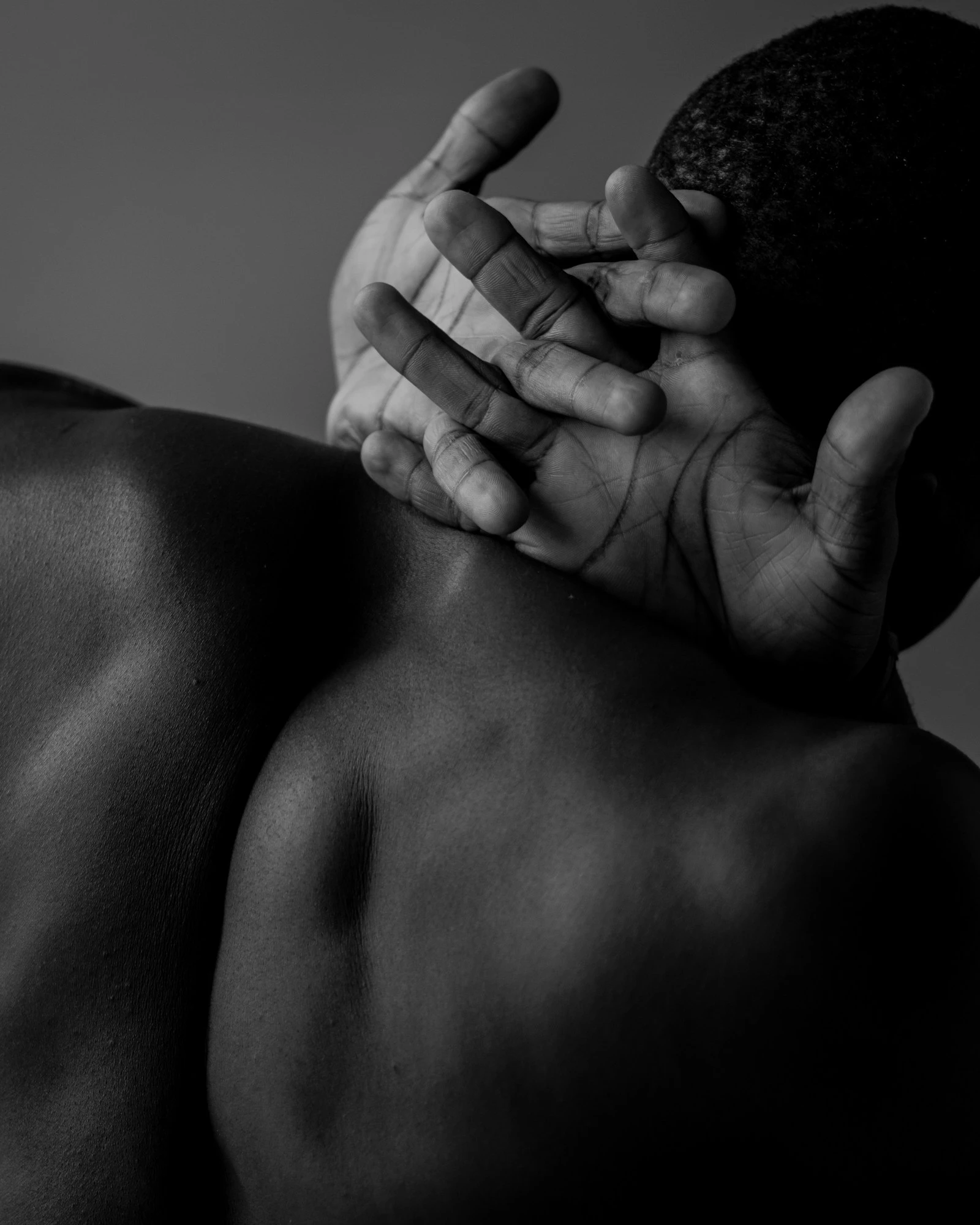 A monochrome photograph of bare shoulders and hands resting behind the neck
